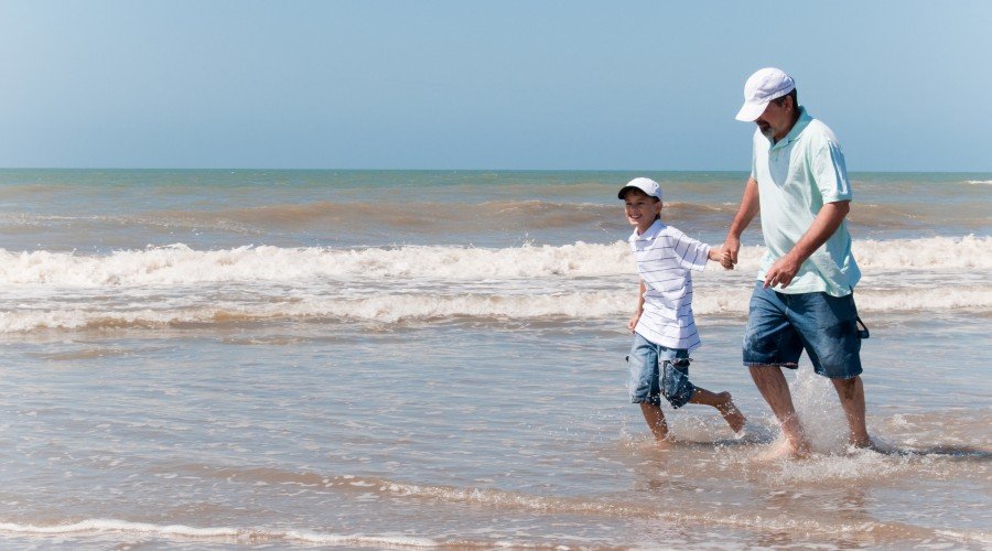 Son and dad walking through water at the beach on Father's Day