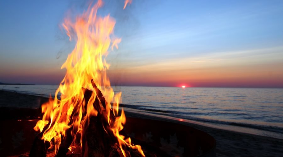 bonfire on the beach with the ocean and sunset in the background