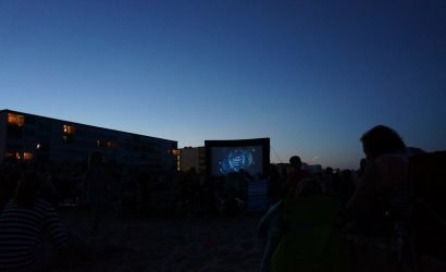 movie screen on the beach with people watching