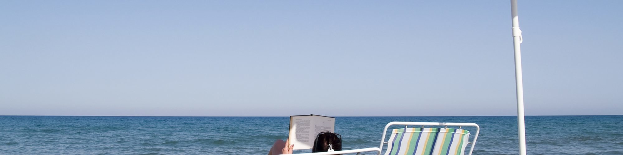 woman reading a book on the beach under umbrella